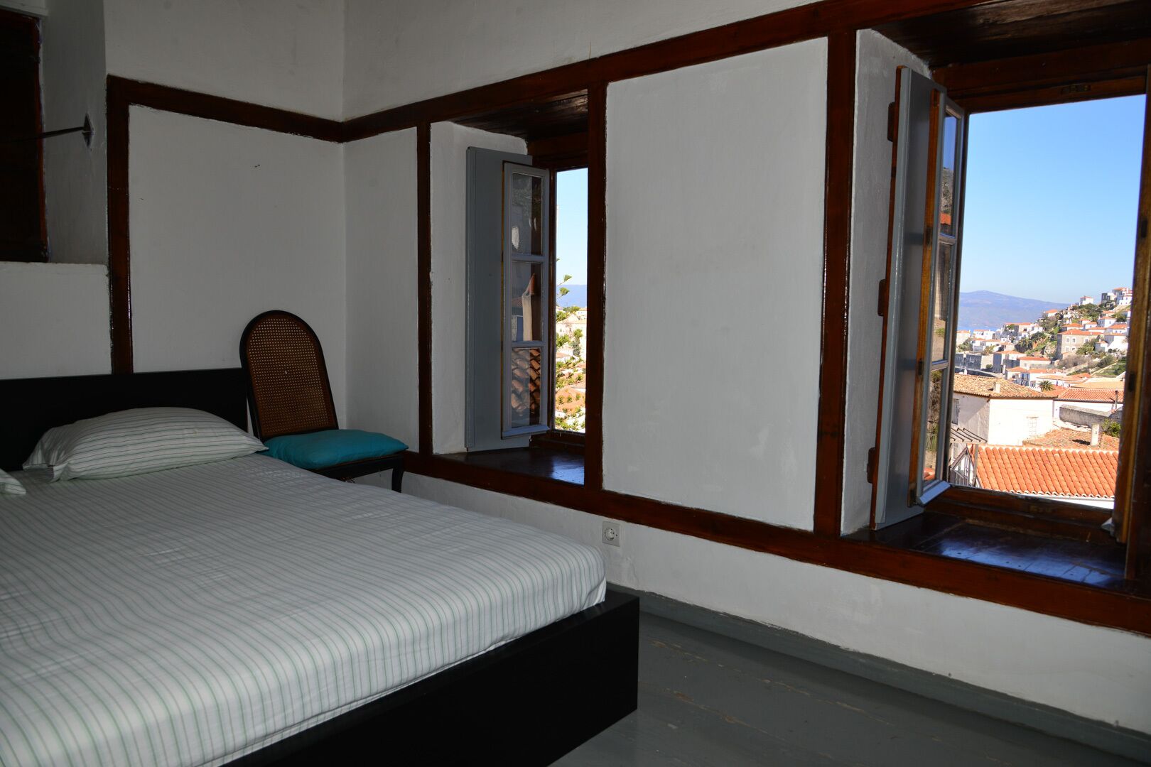 Un dormitorio con cama, mesita de noche y ventana con vistas a un pueblo y montañas.