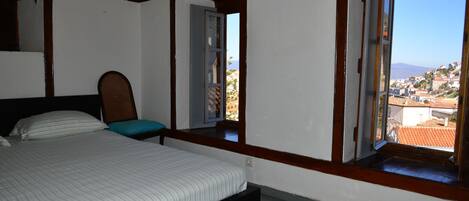 Un dormitorio con cama, mesita de noche y ventana con vistas a un pueblo y montañas.