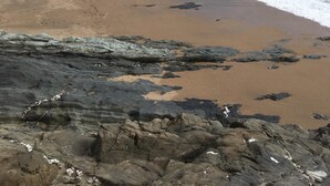 A coastal beach with rocky foreground and waves crashing onto the shore.