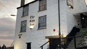 A white building with a sign reading "The Ship Inn" and a staircase leading to the entrance.