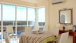 Un coin repas avec une table dressée pour quatre personnes, de grandes fenêtres et une vue sur la mer.