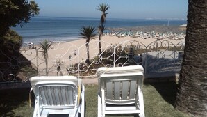 Deux fauteuils blancs, placés face à une plage, avec des parasols et une clôture.