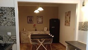 Une cuisine équipée d’une table et de chaises, d’un réfrigérateur et d’un sol carrelé.