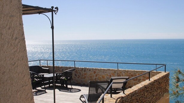 A balcony with stone walls, a wooden deck, and outdoor furniture overlooking the sea. - Residential flat (Ensuès-La-Redonne)