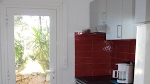 A compact kitchen with white cabinets, a red backsplash, and a coffee maker on the counter. - Residential flat (Ensuès-La-Redonne)