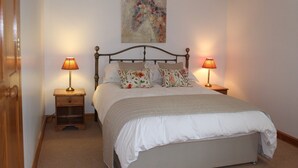 Een netjes opgemaakt bed met bloemenkussens, twee bedlampjes en een schilderij aan de muur.