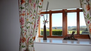 Een kamer met een raam dat uitkijkt op een groen landschap, een vaas met bloemen en een decoratief konijnenbeeldje op de vensterbank.
