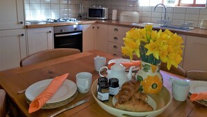 Een keuken met witte kasten, een magnetron en een spoelbak. Er staat een eettafel met borden, een bloevas en een croissant.