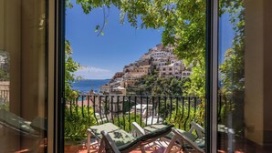 Un balcón con sillas y vistas a un pueblo en la colina y al mar.