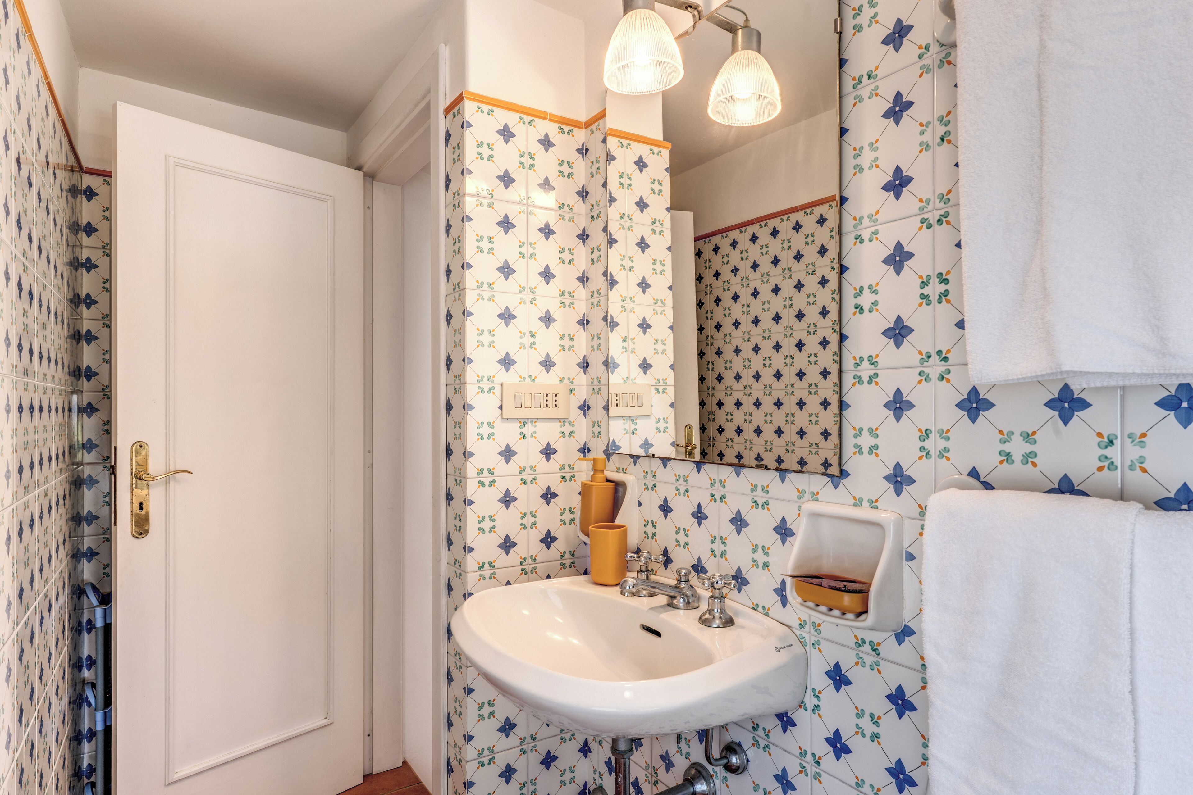 Un baño con un lavamanos blanco, un espejo y un perchero para toallas.