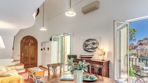 Un comedor con una mesa de madera, sillas, un jarrón con plantas y vistas a la ciudad a través de una puerta abierta.