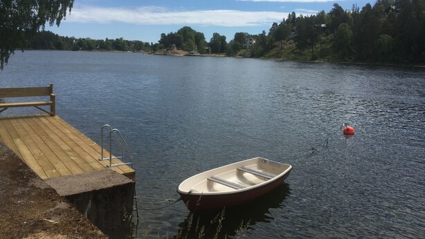 Une jetée en bois avec un bateau amarré, un petit banc en bois et un lac paisible sous un ciel dégagé.