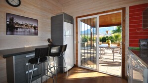 A compact kitchen with a wooden ceiling, a refrigerator, a sink, and a bar area with two stools.