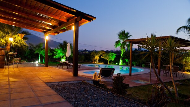 A pool area with lounge chairs and umbrellas, surrounded by palm trees and a covered seating area.