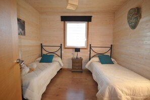 Una habitación con dos camas, paredes de madera, una ventana y una mesita de noche de madera con lámpara.