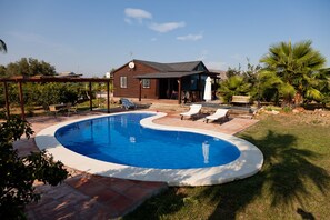 Un patio trasero con piscina, sillas de descanso y una casa de madera.