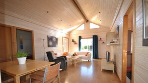 A wooden interior with a dining table, chairs, a sofa, and a TV on a stand.