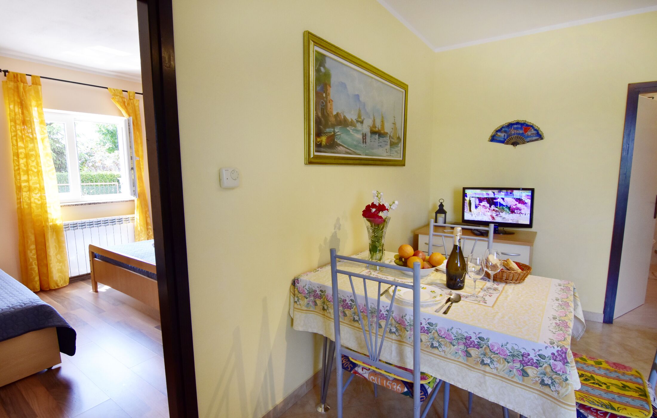 A dining area with a table set for two, a television, and a painting on the wall.