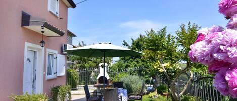 Un patio con una mesa, sillas, un paraguas verde y un horno de ladrillo.
