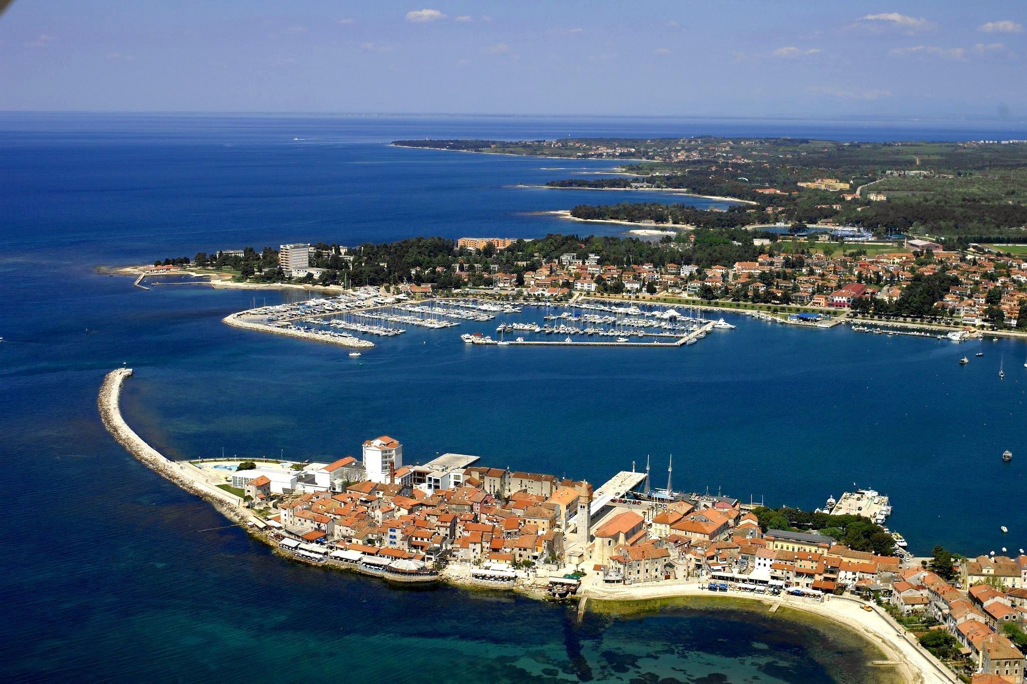 Vue aérienne d’une ville côtière avec un port de plaisance, des bâtiments historiques et un phare.