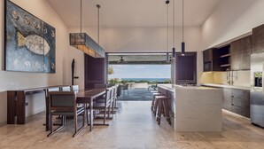 A modern kitchen with a central island, dining area, and a large painting on the wall. - Live Aqua Private Residences Los Cabos (Cabo San Lucas)
