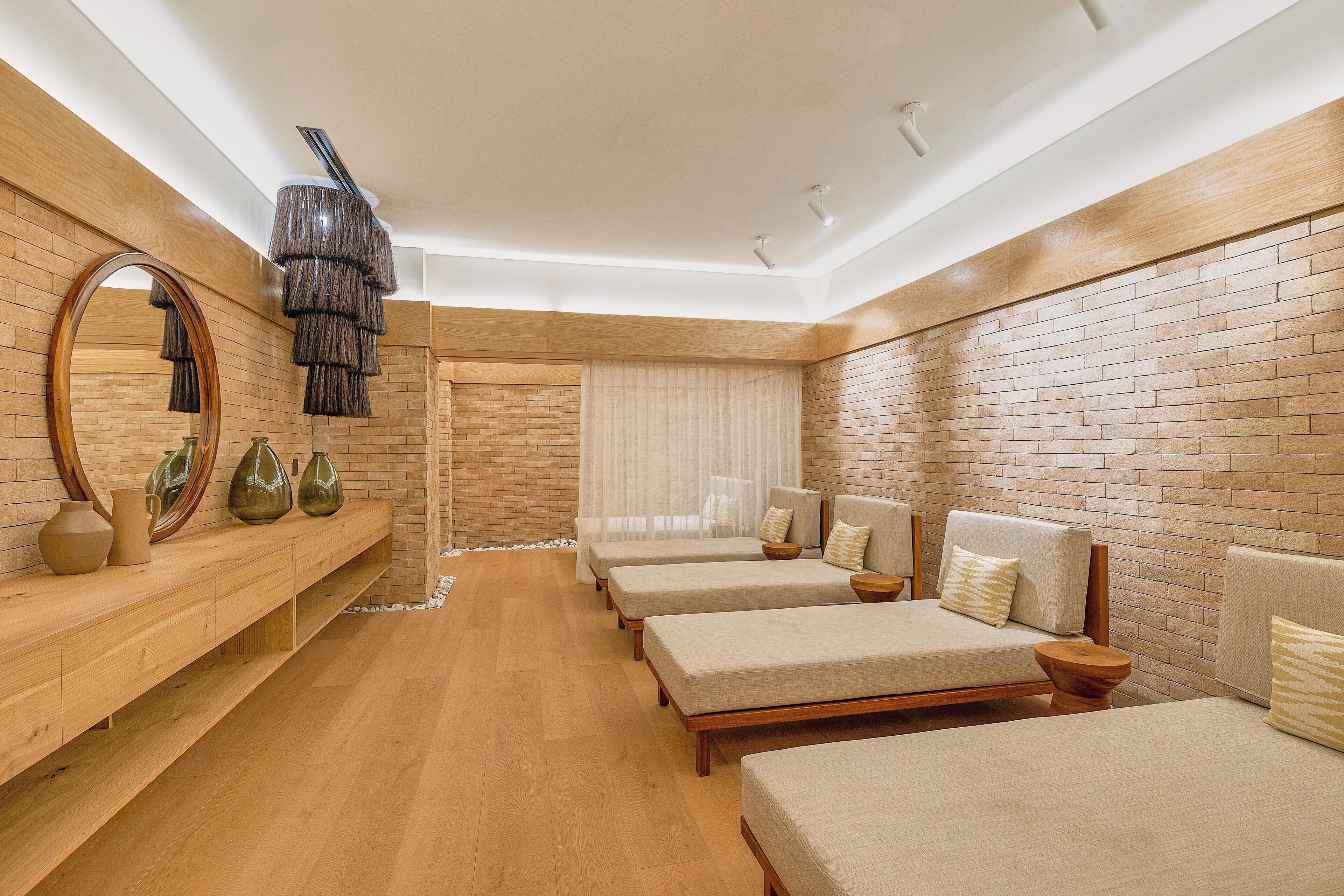 A modern hotel room with a wooden floor, brick walls, and three beds with headboards.