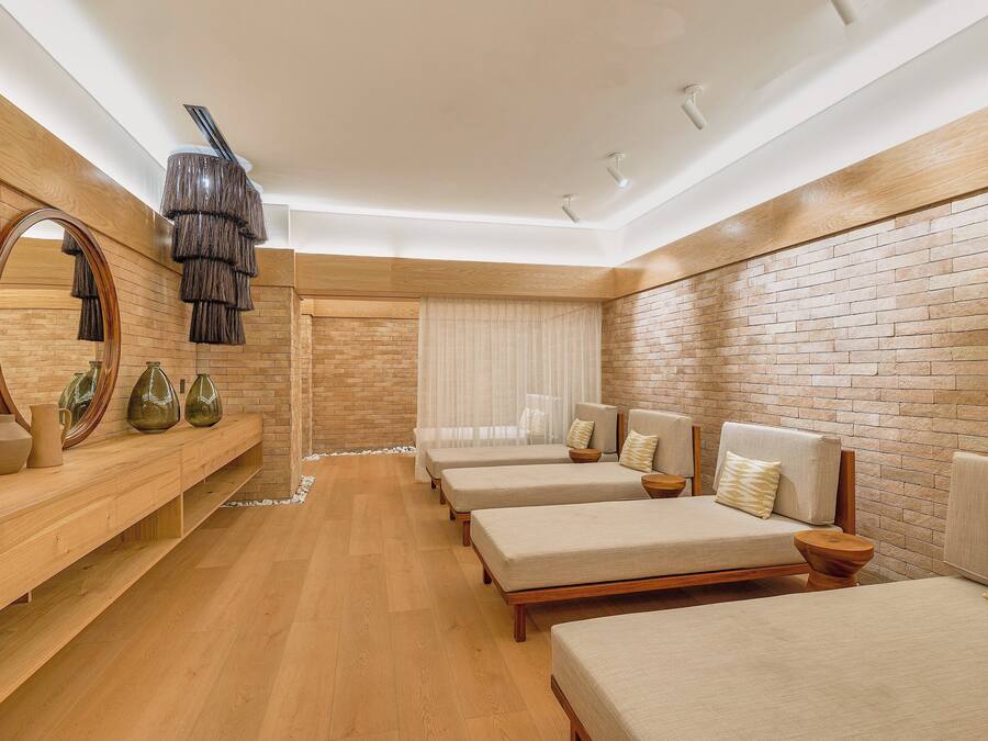 A modern hotel room with a wooden floor, brick walls, and three beds with headboards.