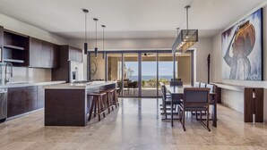 A modern kitchen with a central island, a dining area with a view, and a large painting on the wall. - Live Aqua Private Residences Los Cabos (Cabo San Lucas)