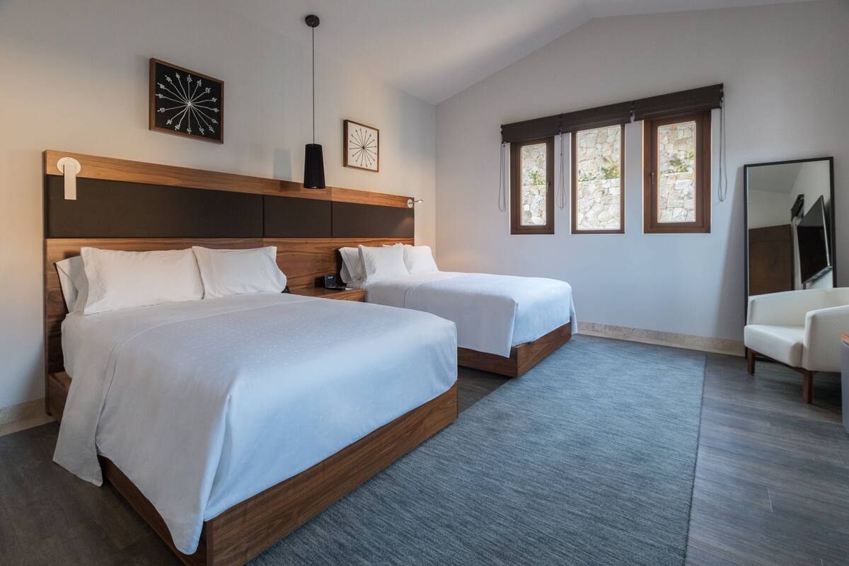 Une chambre d’hôtel moderne avec deux lits, un grand miroir et une vue sur l’extérieur par les fenêtres.