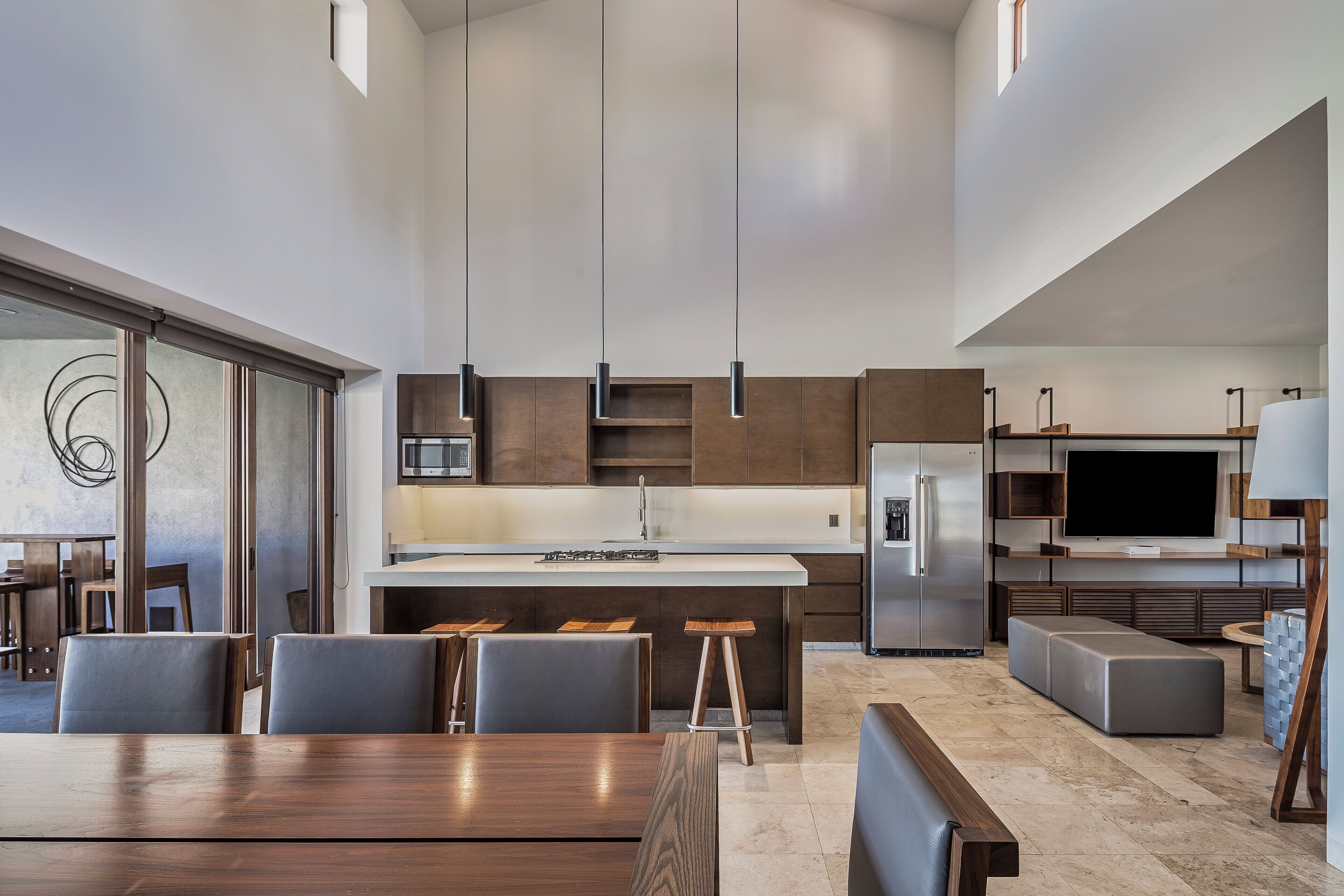 A modern kitchen with a central island, bar stools, and a dining area with a wooden table and chairs.