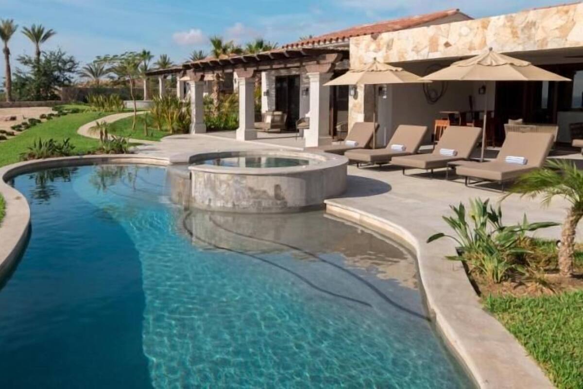 Une piscine au design incurvé, un espace patio avec des chaises longues et un bâtiment en pierre doté de colonnes.