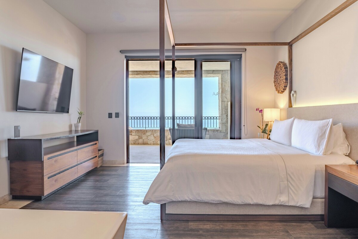 A hotel room with a bed, a TV, a dresser, and a balcony with a view.