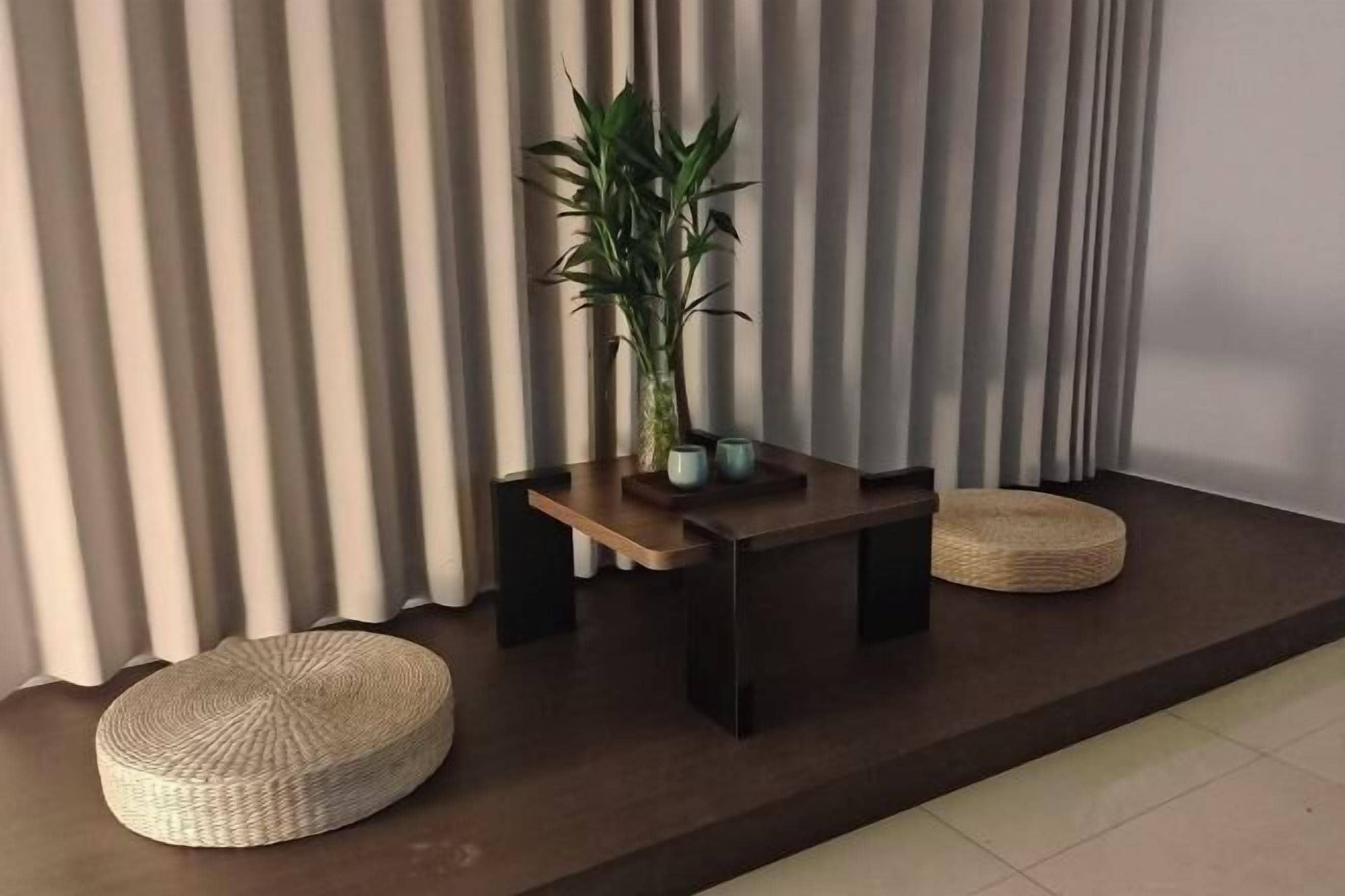 A modern room with a dark wooden table, a potted plant, and two woven poufs.