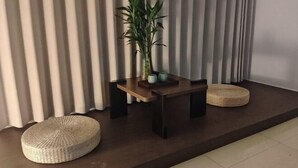 Quarto moderno com mesa de madeira escura, um vaso de planta e dois pufes trançados.
