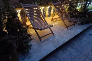 Two wooden lounge chairs with metal frames, positioned on a tiled patio with potted plants and a stone wall in the background. - Sha.heyue. Hotel (Emeishan City)