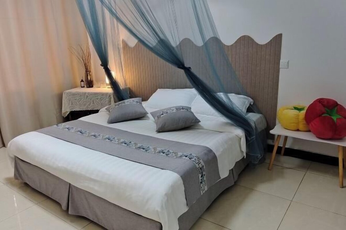 A neatly made bed with a canopy, a bedside table with a vase, and a wall-mounted light fixture.