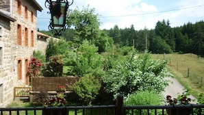 A stone building with a balcony, a wooden fence, and a pathway leading through a garden with various plants and flowers. - Country Cottage / Gite - Usso, en Forez (Usson-En-Forez)