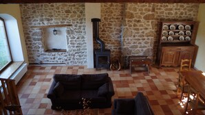 A cozy living room with a stone wall, a fireplace, a sofa, and a cabinet with decorative plates. - Country Cottage / Gite - Usso, en Forez (Usson-En-Forez)