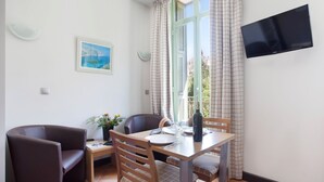 Un comedor con una mesa lista para dos personas, una silla de cuero marrón, una silla de madera, una mesita con una planta y un cuadro en la pared.