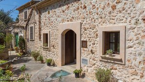 Un bâtiment en pierre, doté d’arcades au niveau des portes et des fenêtres, d’une petite piscine et de plantes en pot.