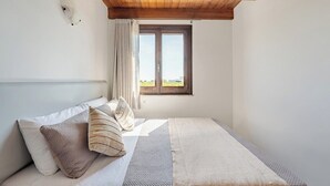 A bedroom with a wooden ceiling, a bed with pillows, a window with curtains, and a view of greenery outside. - House / Villa - MarsalaHouse with garden (Marsala)