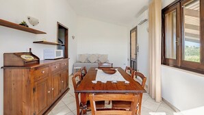 A dining area with a wooden table, chairs, a cabinet, a microwave, and a sofa. - House / Villa - MarsalaHouse with garden (Marsala)