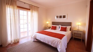A hotel room with a large bed, two bedside tables with lamps, a window with curtains, and a small artwork above the bed. - Luxury 4 bedroom villa with private pool on 5* golf & beach resort (Obidos)