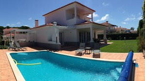 A swimming pool with a tiled deck, lounge chairs, and a covered patio area. - Luxury 4 bedroom villa with private pool on 5* golf & beach resort (Obidos)