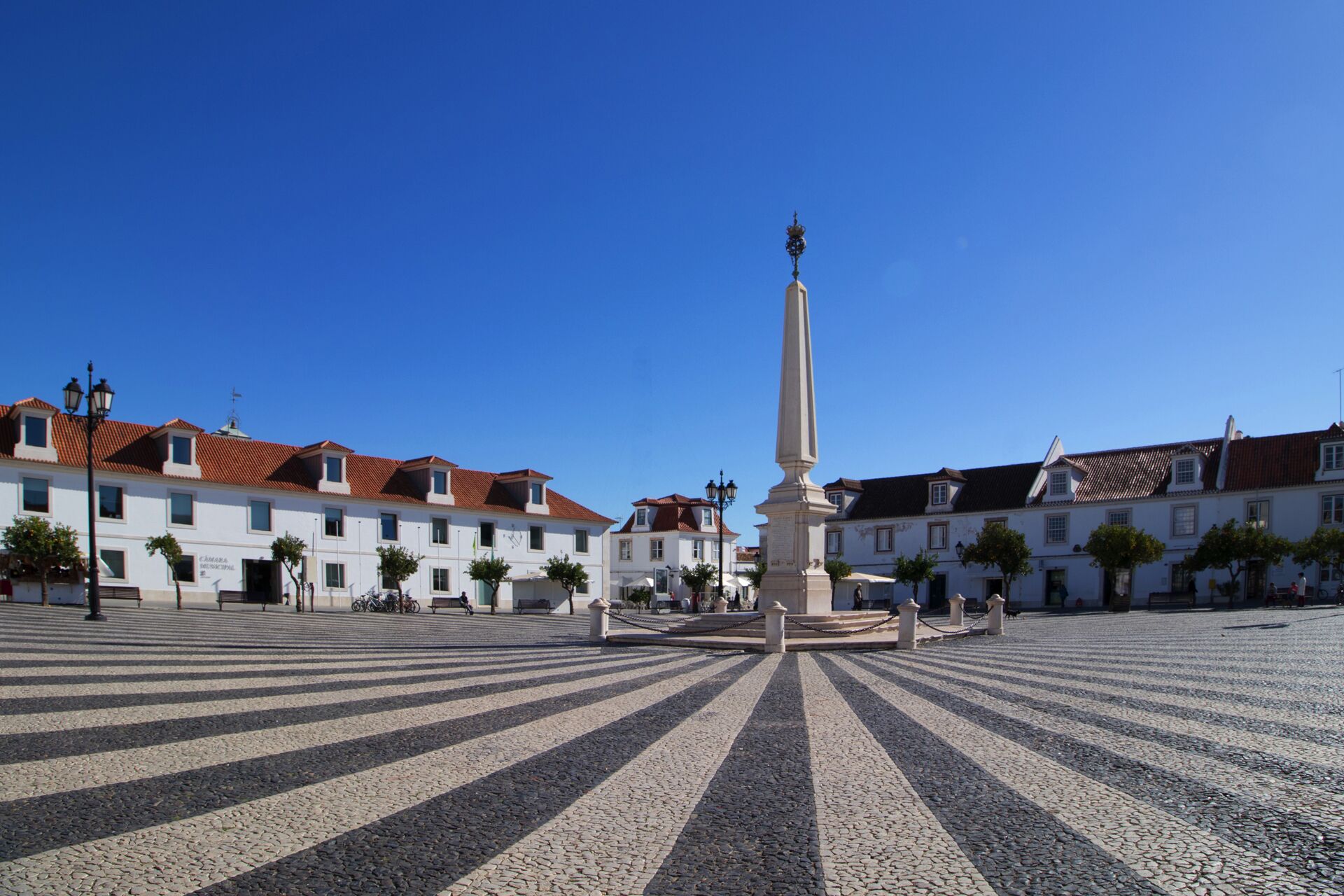 Una plaza con un monumento central, rodeada de edificios con tejados de tejas rojas.