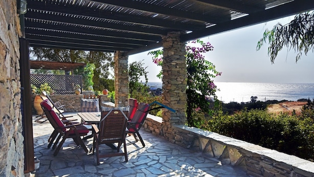 An outdoor patio with stone flooring, a wooden table, and red cushioned chairs. - Family house with a sea view for rent in the area of Koundouros (Kea)
