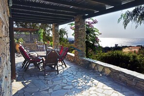 An outdoor patio with stone flooring, a wooden table, and red cushioned chairs. - Family house with a sea view for rent in the area of Koundouros (Kea)