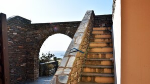 A stone staircase leading up to an arched stone bridge, with a view of the sea in the background. - Family house with a sea view for rent in the area of Koundouros (Kea)