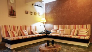 A living room with a sectional sofa, a round coffee table, and a lamp. - Family house with a sea view for rent in the area of Koundouros (Kea)