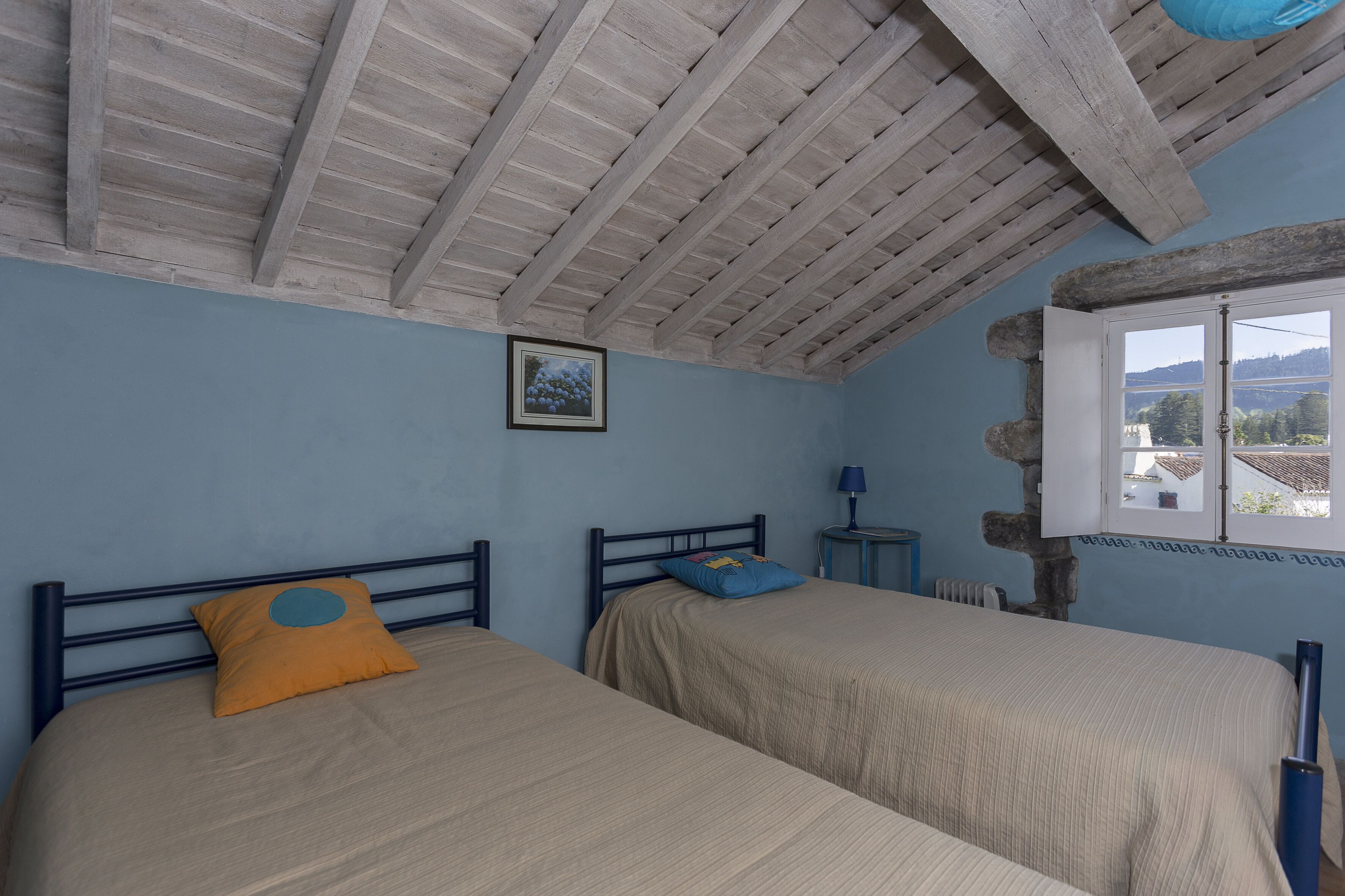 Une chambre avec deux lits, une fenêtre donnant sur un beau paysage et un plafond rustique.